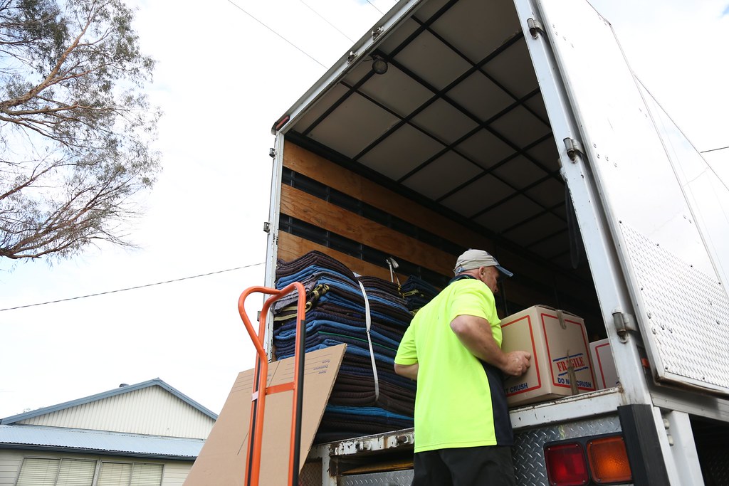 Mover stacking labelled cardboard boxes and padded furniture blankets inside a removal truck