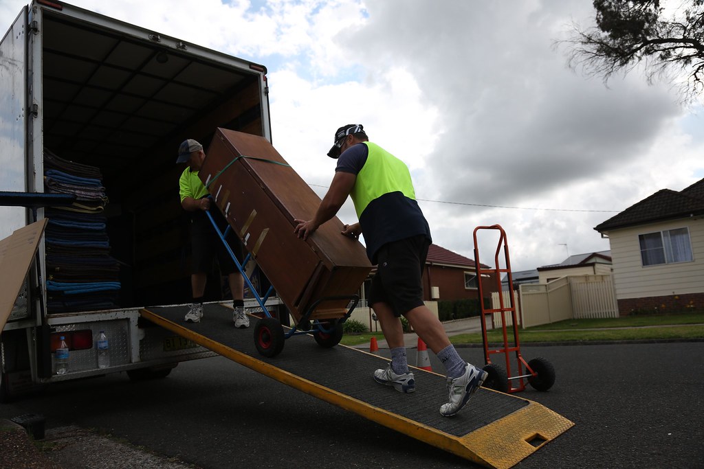 Removalists pushing furniture on a trolley up a ramp into a removal truck