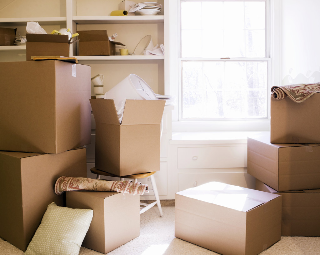 Bright room filled with sealed cardboard moving boxes, wrapped items and household goods ready for moving day
