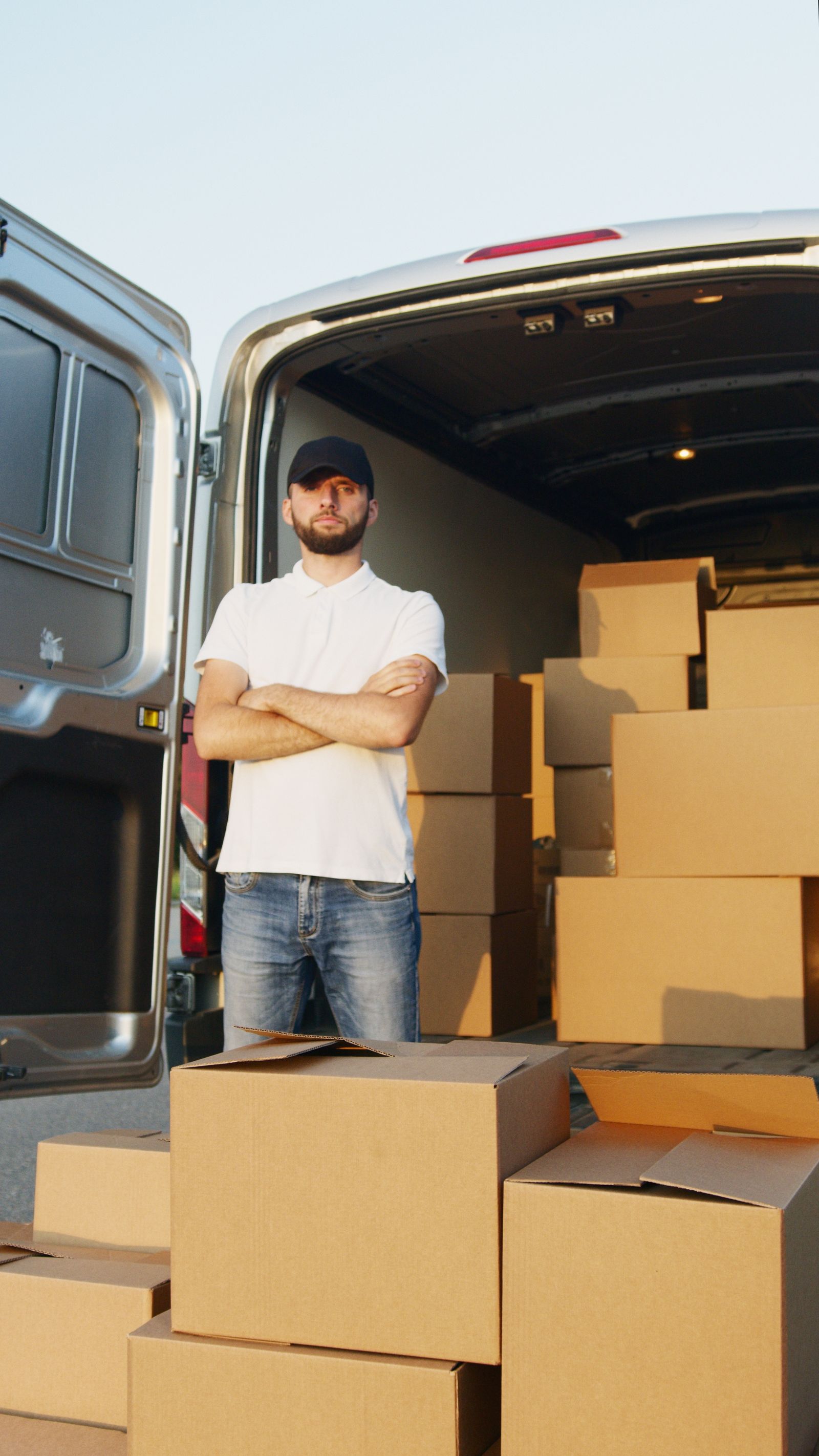 Removal worker standing beside a van loaded high with stacked moving boxes