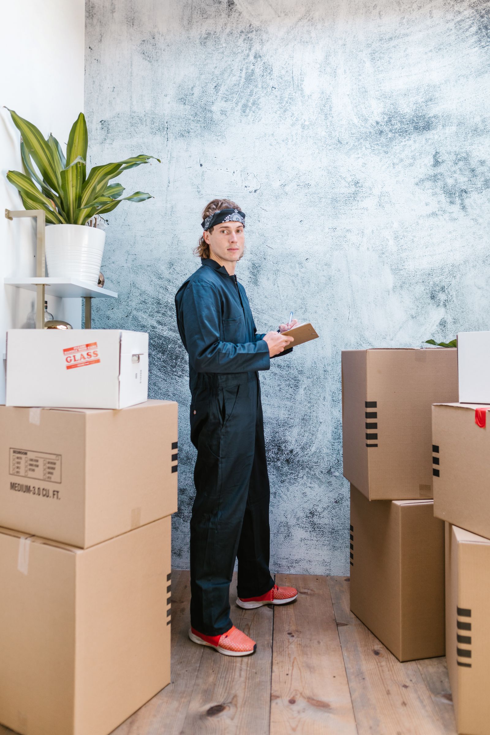Professional mover in coveralls checking an inventory clipboard between labelled moving boxes