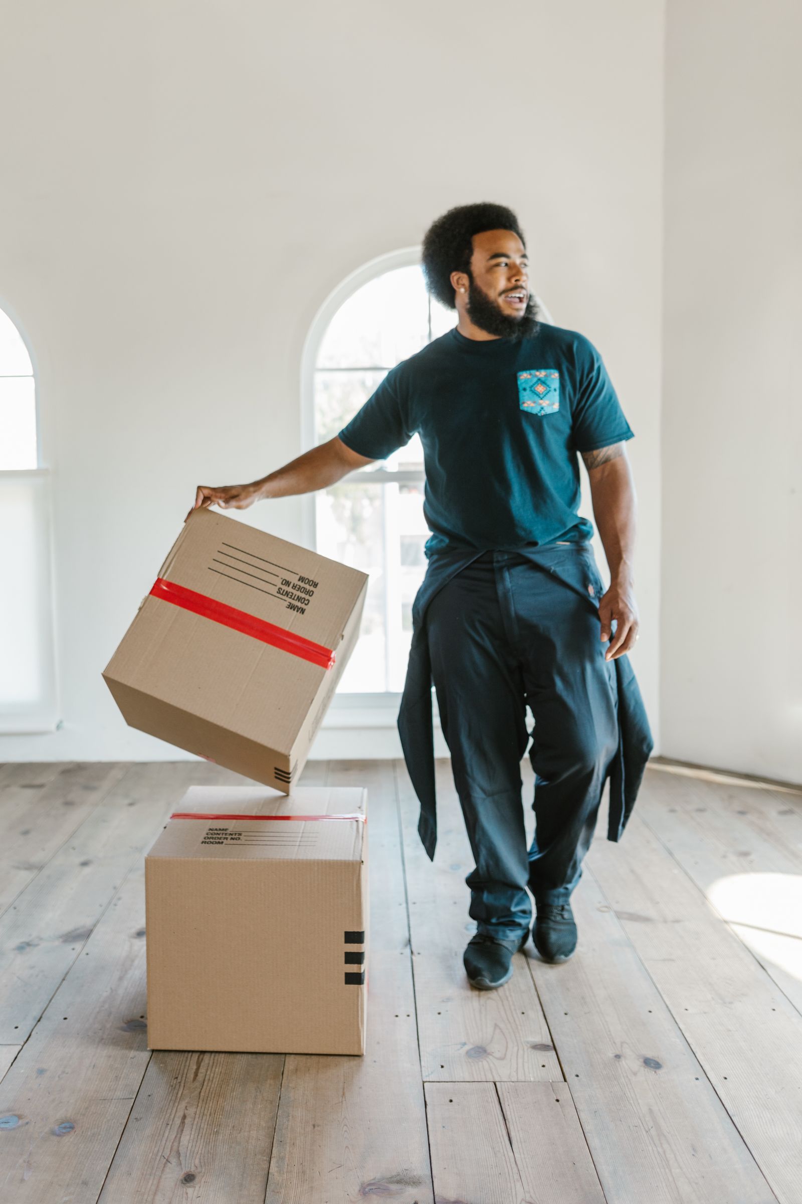 Mover carrying a sealed cardboard box through a bright empty room on moving day
